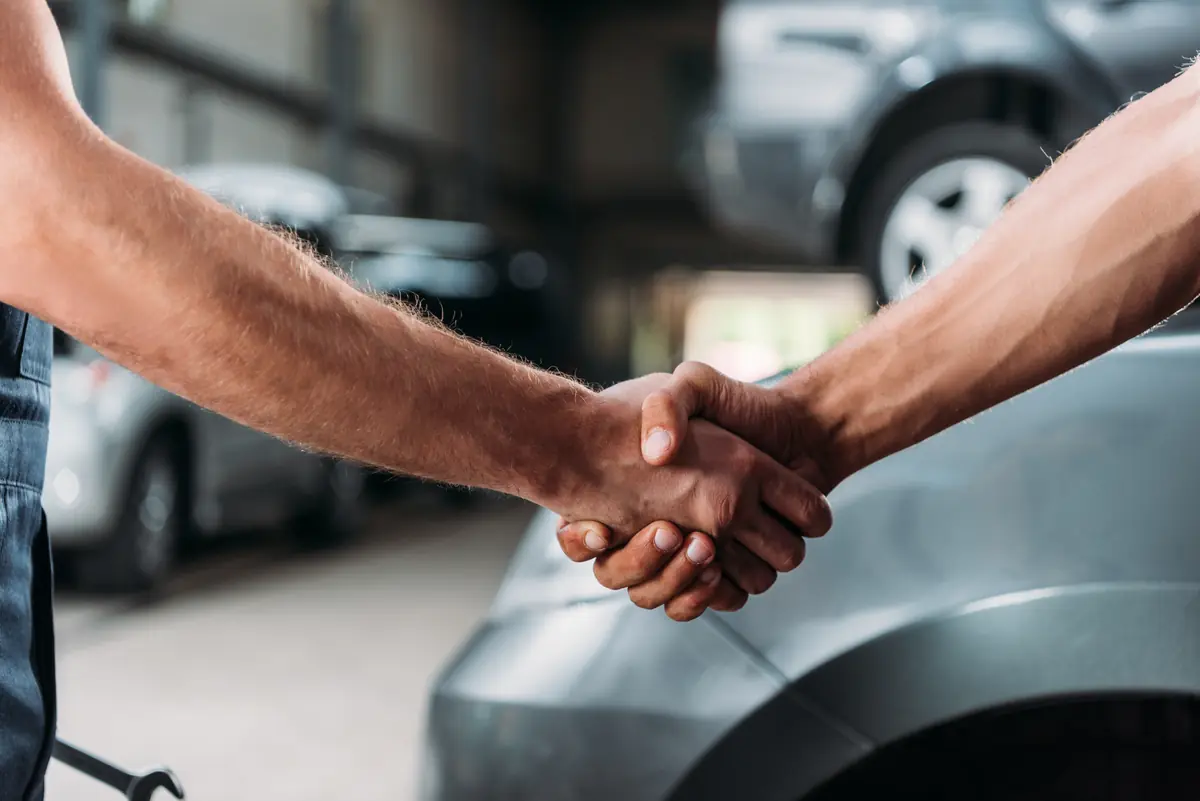 Aperto de mãos entre o mecânico e o cliente na oficina