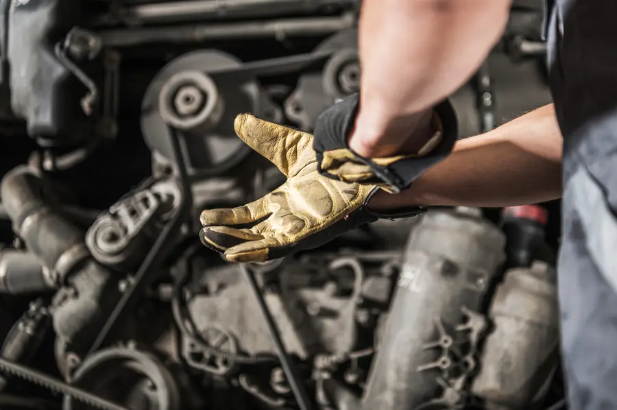 Mecânico com luvas segurando peça no compartimento do motor